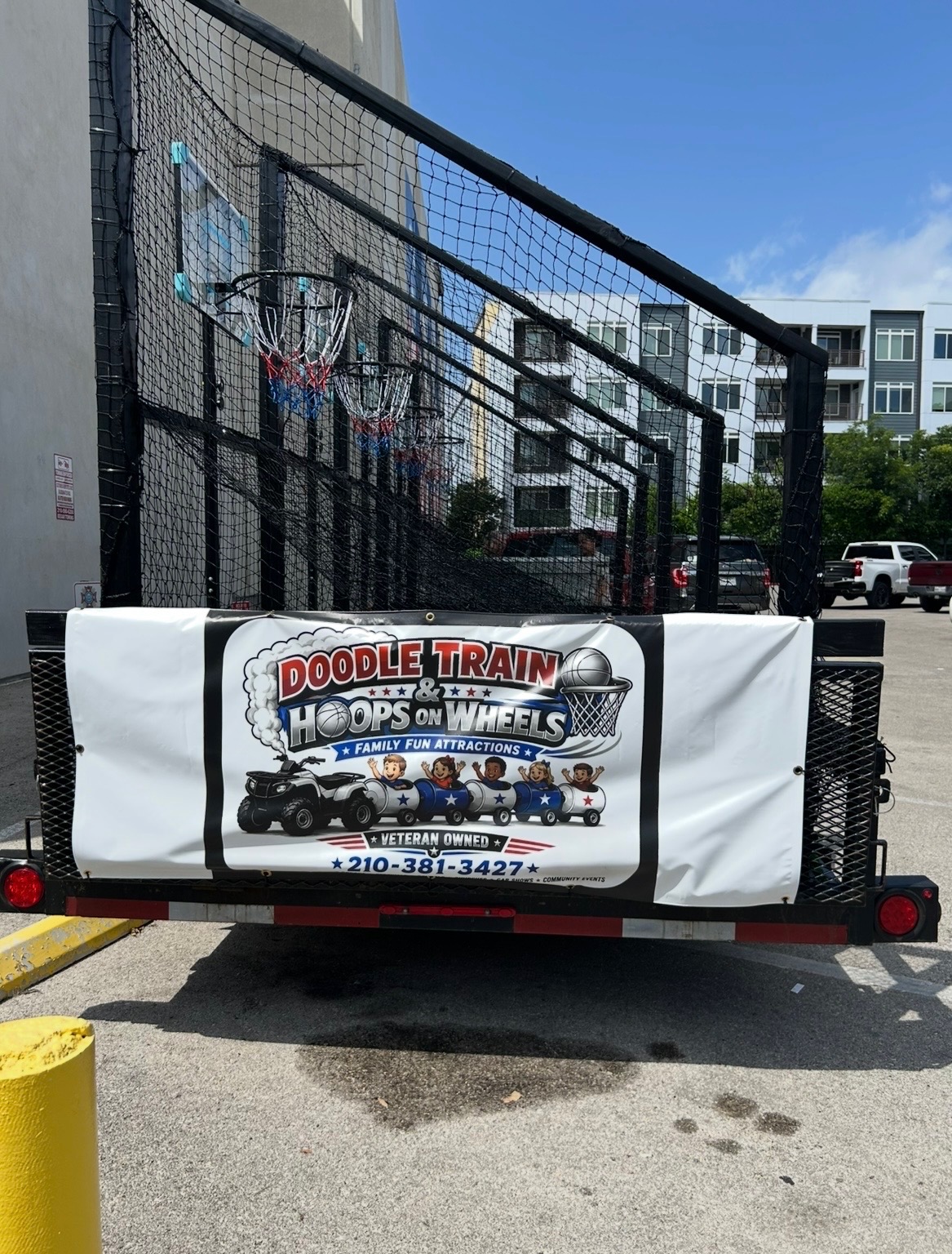 Rear view of the trailer showing the Doodle Train and Hoops on Wheels family fun attractions banner, veteran owned, phone 210-381-3427
